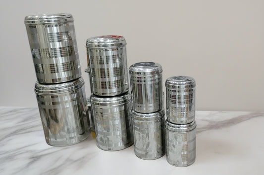 A set of stainless steel storage containers of varying sizes arranged together, commonly known as a 'dabba' or 'bartan'.